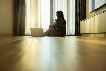 Good looking middle aged woman with laptop sitting on floor lets sunlight into living room on morning in modern, enjoy carefree rest and optimistic mood. Wealthy house. Well-being. Space for text