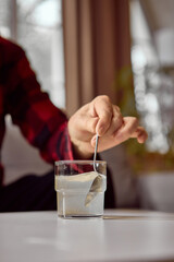 Hand stirring dissolved medicine powder in glass of water with spoon. Concept of instruction...