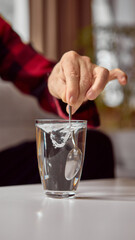 Hand stirring clear water in glass with metal spoon on white table. Concept of instruction visuals, pharmacy education, and health awareness materials.