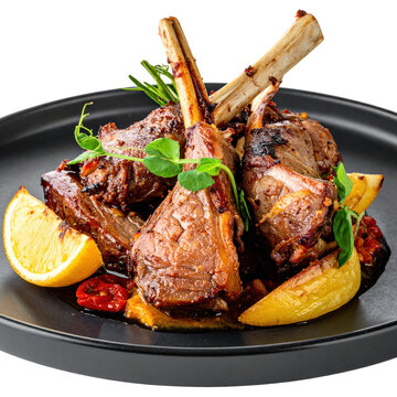 Grilled cabrito assado roast goat with lemon wedges and rosemary on a black plate isolated white background