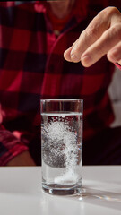 Older man dropping tablet into water glass creating dissolving bubbles. Concept of pharmacy materials, healthcare promotion, and home wellness guidance.