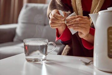 Elderly woman opening medicine sachet above steaming glass of hot water. Concept of pharmacy instruction, wellness education, and patient healthcare awareness.