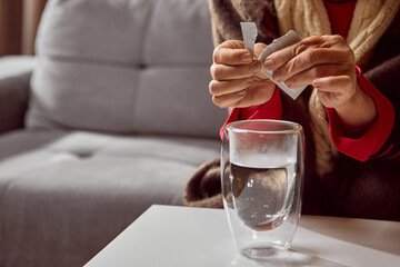 Senior woman opening white sachet above hot water in double wall glass. Concept of pharmacy product preparation, dosage learning, and healthcare education.