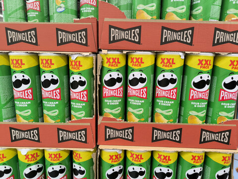 Pringles Sour Cream & Onion XXL Pack cans in cardboard carriers | Mr. Pringle mascot & red logo | Concept of snack food industry, consumer goods, retail editorial