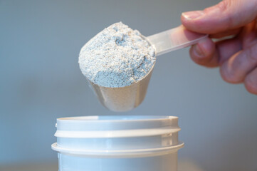 Close-up of someone putting a scoop with protein powder in a shaker bottle.