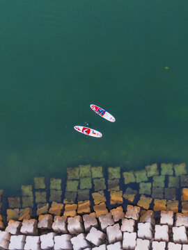 Aerial view of two paddleboards glide across the tranquil turquoise waters near the contrasting geometric concrete blocks lining the shore, Progreso, Yucatan, Mexico.