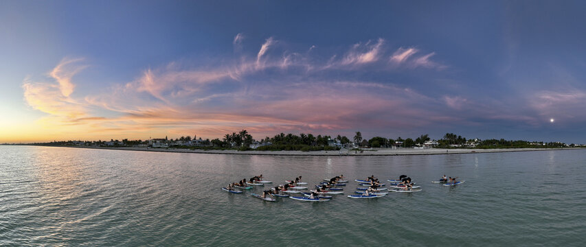 Aerial view of a yoga class practicing poses on paddle boards in the tranquil waters, under a vibrant sunset sky over Progreso coastline, Progreso, Yucatan, Mexico.
