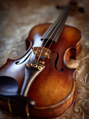 close-up of polished wooden violin with warm brown finish resting on patterned fabric surface, showcasing f-holes, bridge, strings, tailpiece, and chinrest in elegant classical composition