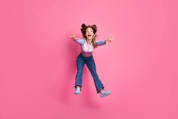 Excited young woman jumping joyfully on a bright pink background expressing happiness and...