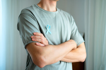 Man standing with crossed arms wearing blue satin ribbon on shirt. Concept of prostate cancer awareness in November, prevention, early diagnosis, and medical care for mens health.