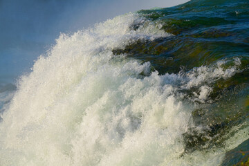 A detailed view of the American Falls at Niagara Falls State Park, New York, capturing the texture and power of rushing water as it plunges over the cliff in bright sunlight