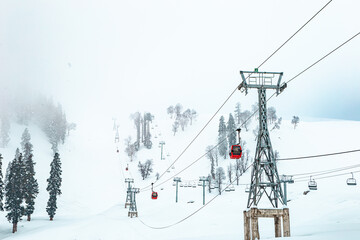 Aerial view of a snow-covered mountain landscape dotted with ski lifts carrying vibrant red gondolas against the stark white backdrop, Gulmarg, Jammu and Kashmir, India.