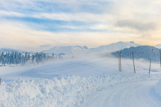 Aerial view of snow-covered fields and mountains, with trees dusted in white and a winding road cutting through the drifts, Rovaniemi, Finland.