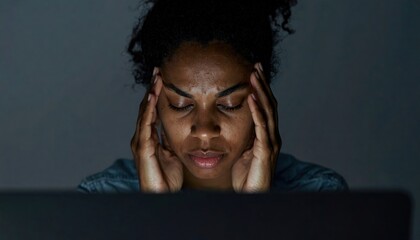 Woman rubbing temples at laptop late at night — digital fatigue and stress from overwork