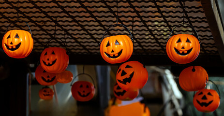 Orange pumpkins with scary faces decorated for Halloween hanging from a ceiling on local market