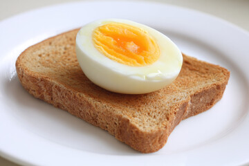 Fototapeta premium Slice of toasted bread and boiled egg half rest on white plate, creating simple breakfast meal with warm and inviting appearance