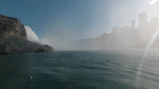Forward-moving shot on the river approaching Niagara Falls. Dark teal water twists and foams while the cliffside vanishes into white mist. Power, scale, danger as nature drowns everything in spray.