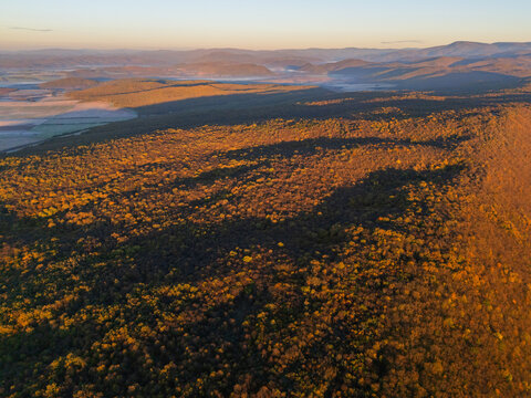 Aerial view of Slovensky kras mountains ablaze with autumnal hues, casting long shadows as dawn breaks, painting the landscape with warmth and serenity, Plesivec, Kosice Region, Slovakia.