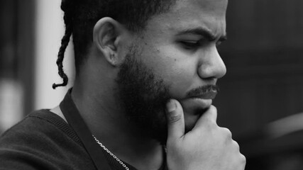 Side view of a thoughtful black man with braided hair resting hand on chin, deep in reflection, focused expression, urban outdoor setting, monochrome close-up - Powered by Adobe