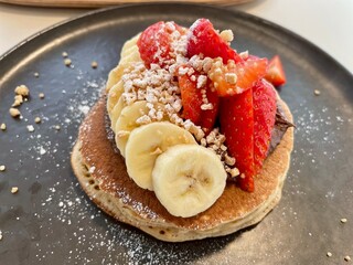 Delicious pancakes with fresh strawberries and banana slices on a plate, sweet breakfast or dessert.