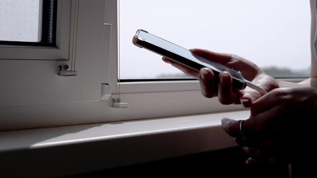 A close-up view of hands disconnecting a charging cable from a smartphone near a bright window. The focus is on the connection and disconnection process, highlighting modern mobile device usage