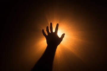 Silhouette of a hand reaching toward a glowing light, symbolizing ambition, hope, and aspiration.
