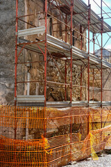 Close view of metal scaffolding in front of a crumbling stone facade during building restoration.