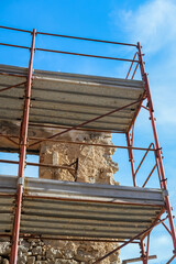 Metal scaffolding platforms and guardrails rise against a bright blue sky at a construction site.