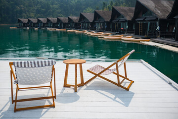 wooden beach chair and coffee table on white raft and swimming pool at waterfront of the open water in natural lake