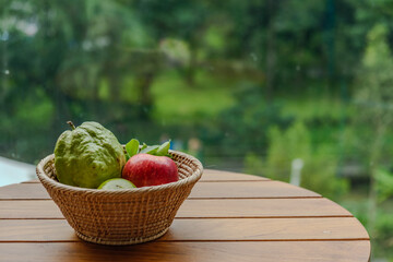 top view photograph of small basket of fruit included with apple orange and guava on the wood table in sunshine