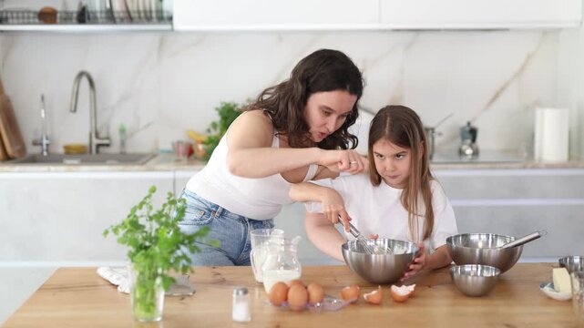 Happy mother and her daughter whisking ingredients in a bowl using metal corolla in the kitchen
