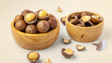 Macadamia nuts with shell  in wooden bowls with broken macadamia and tool on beige background