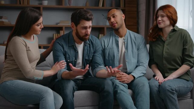 Four multiethnic friends supporting calming sad man at home party on sofa stress worried male talking difficulty health problem bankruptcy breakup life trouble group men women listening support trust