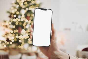 Phone mockup in hand over christmas tree, stars, gifts and decoration, Mobile phone with blank white phone screen, Winter holiday online shopping and advertisement concept