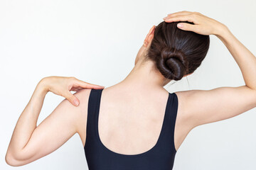 Young brunette woman performing neck stretching exercises, gently tilting her head to the side to stretch her neck muscles. Back view
