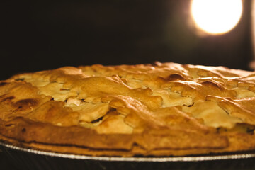 Closeup of a pie baking inside a warm oven with the glow of the lightbulb in the background. Golden crust, perfect for holidays and cooking themes