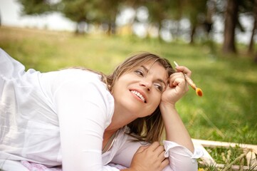 Fototapeta premium Woman relaxing on grass while painting outdoors in a sunny park surrounded by trees