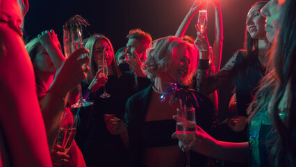 New Year party with smiling friends holding champagne glasses under warm lights. Concept of alcohol brand visuals, nightlife advertising, friendship emotion, and celebration lifestyle