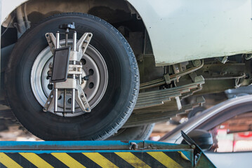 Close-up of a car wheel during alignment service on a lift in an auto repair shop, showing professional adjustment equipment attached to the tire.