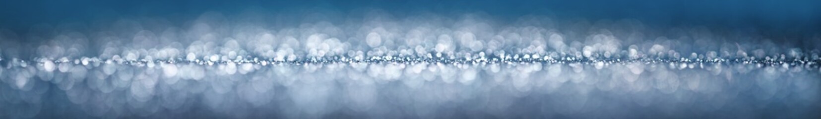 Blue and silver glitter blur as wide banner background. Abstract studio shot with beautiful fantasy bokeh circles.