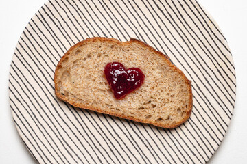 Close up of Slice of whole wheat sourdough bread with Heart Shaped Jam on Striped Plate