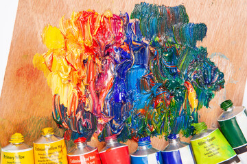Vibrant oil paints mixed on a wooden artist's palette with tubes of color in the background. A...
