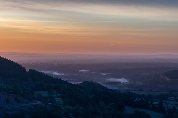 Soft morning mist settling over a forested valley at sunrise