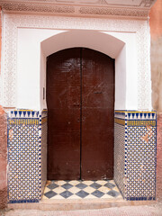 Historic Moroccan Doorway in Marrakech Showcasing Elaborate Stucco Reliefs, Vibrant Geometric Zellij Tiles, and Dark Wooden Arch.