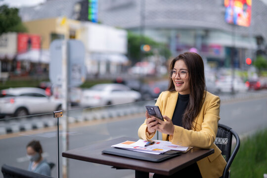 Businesswoman using smartphone and smiling at outdoor cafe - Powered by Adobe