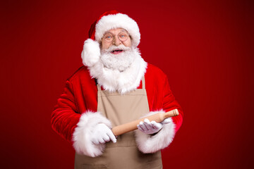 Santa in a festive red suit with a beige apron and rolling pin smiling warmly against a bright red background perfect for Christmas marketing