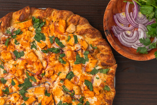 Pizza topped with spicy buffalo chicken chunks, red onion slices, and fresh cilantro on a golden crust.