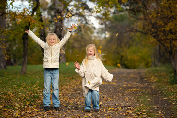 Fototapeta premium Two happy sisters are playing with yellow leaves in autumn park.