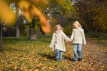 Fototapeta premium Two sisters walking through an autumn park holding hands. Warm natural light and fall colours create a dreamy, emotional atmosphere of childhood and nature.