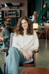 Relaxed woman sits in a wooden chair in a modern cafe with casual lifestyle vibe